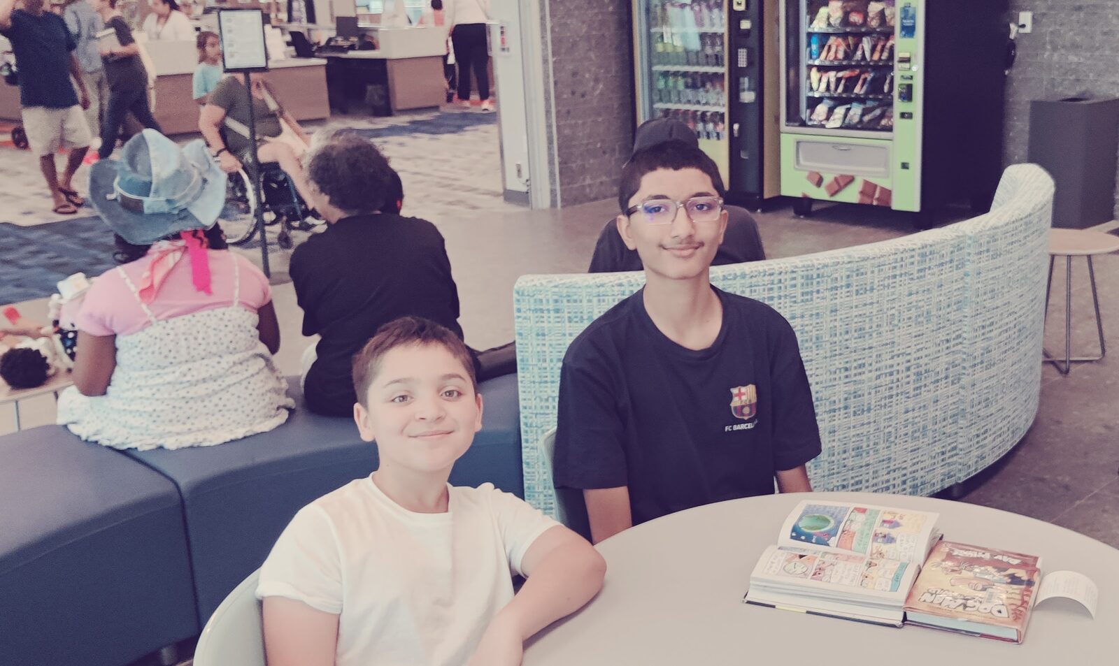 Two students smiling at the camera with an open workbook on the table in front of them.