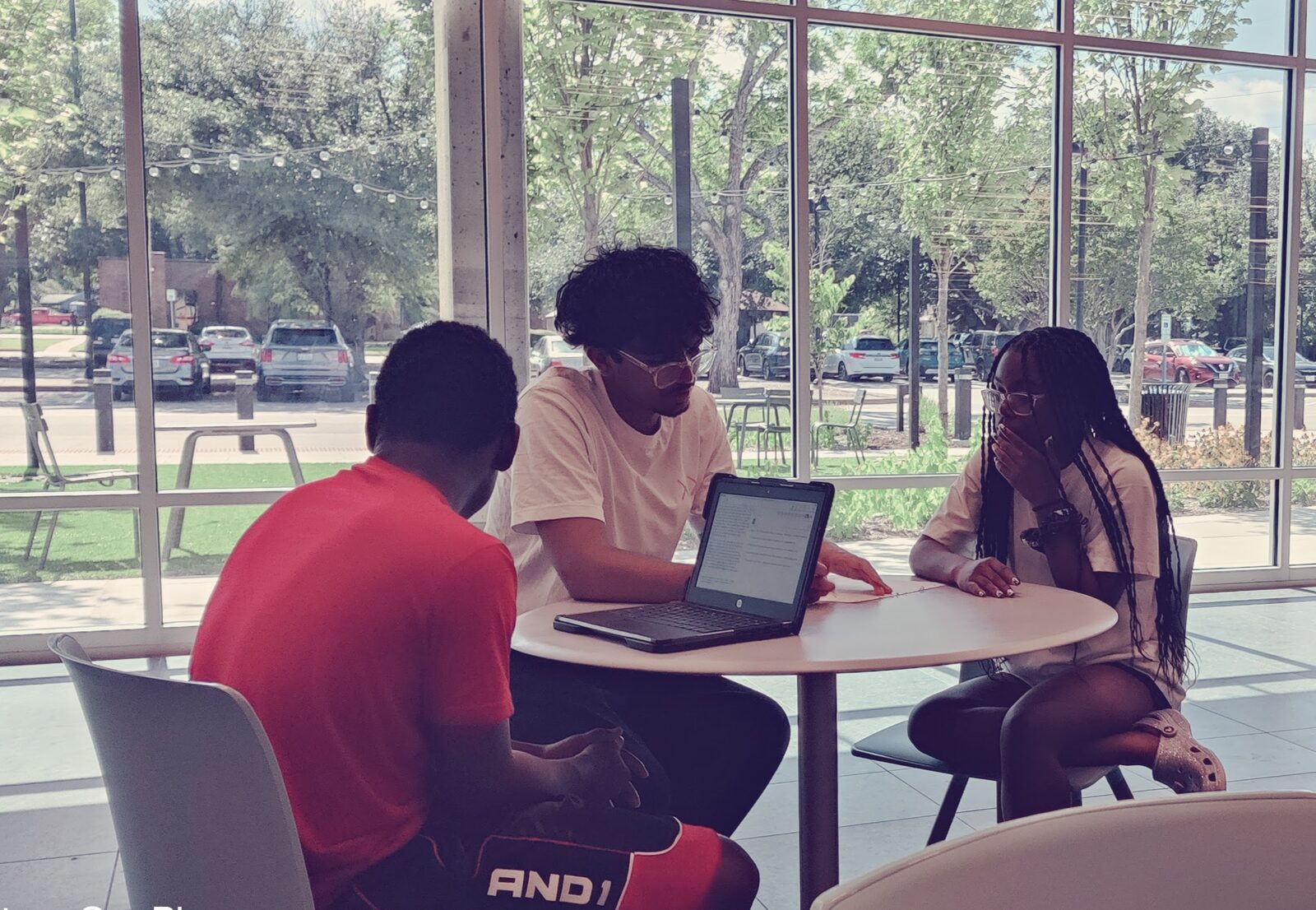 An Eleos tutor works through a problem on a laptop with two students at the Garland Public Library.